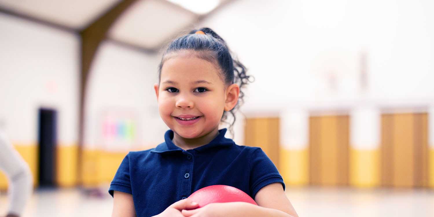 Smiling student holding ball in school gym.
